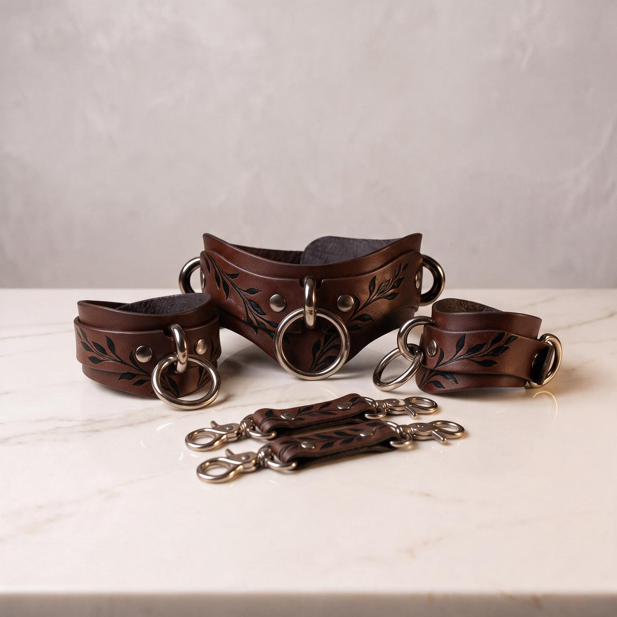 A set of brown leather straps with leaf designs, arranged on a white marble surface.