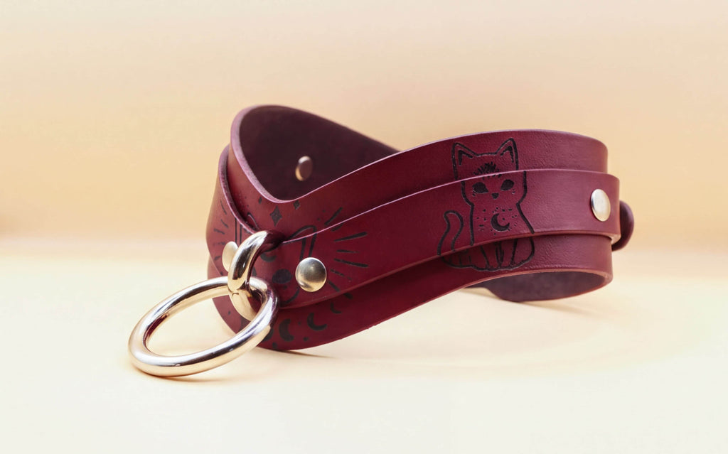 A burgundy leather choker necklace with a cat design and metal rings.