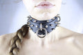 A close-up of a person's neck and chin wearing a black leather choker necklace with spikes and a ring.