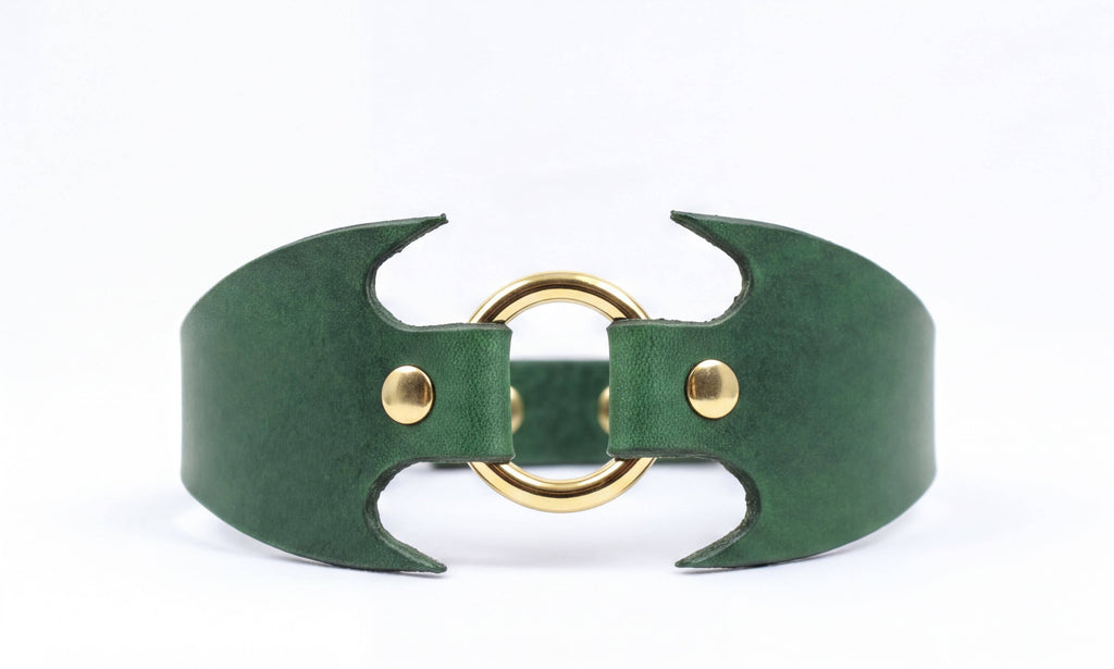 A green leather cuff with a gold ring and two gold buttons.