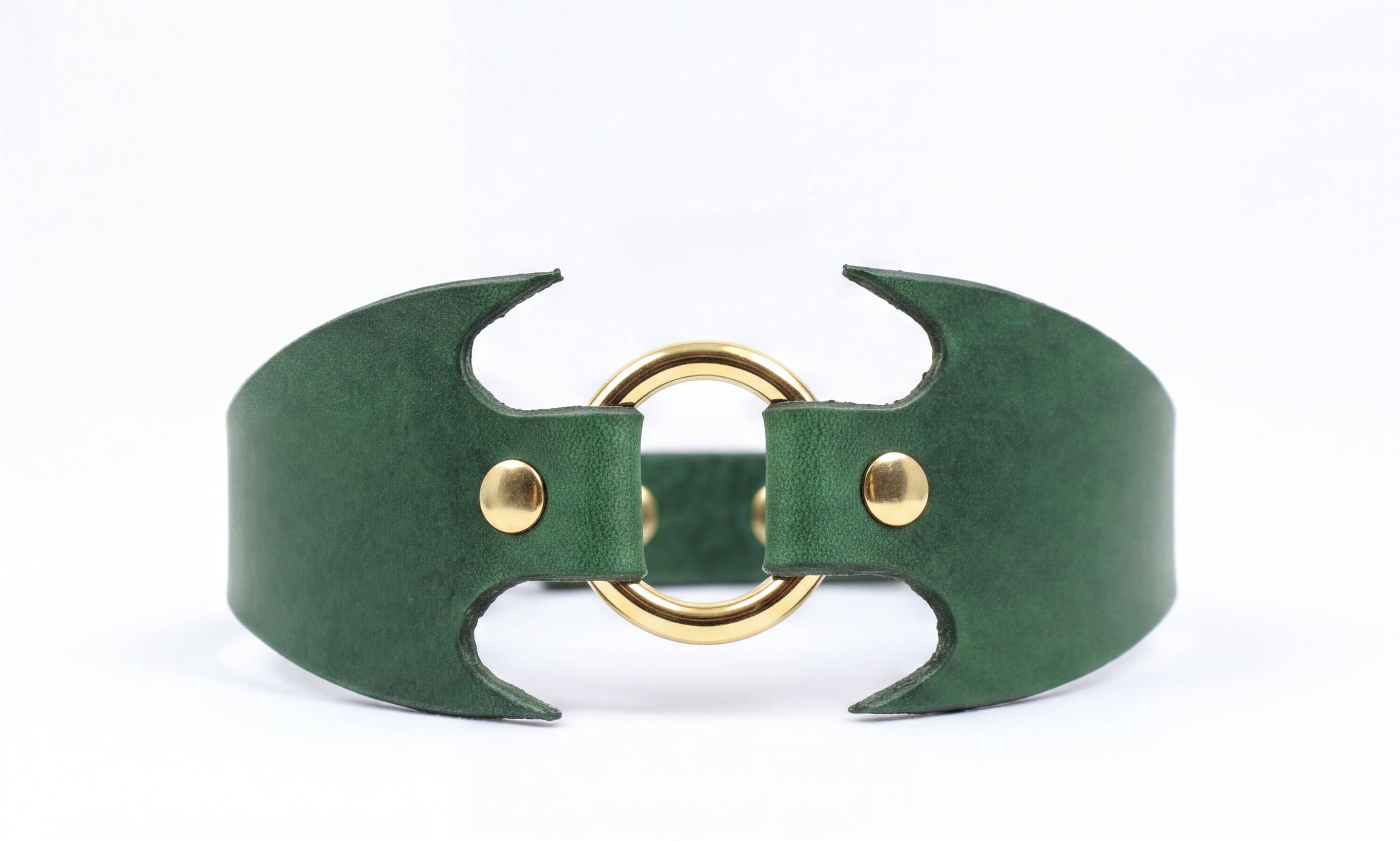A green leather cuff with a gold ring and two gold buttons.