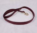 A burgundy leather dog leash with a gold heart-shaped charm attached.