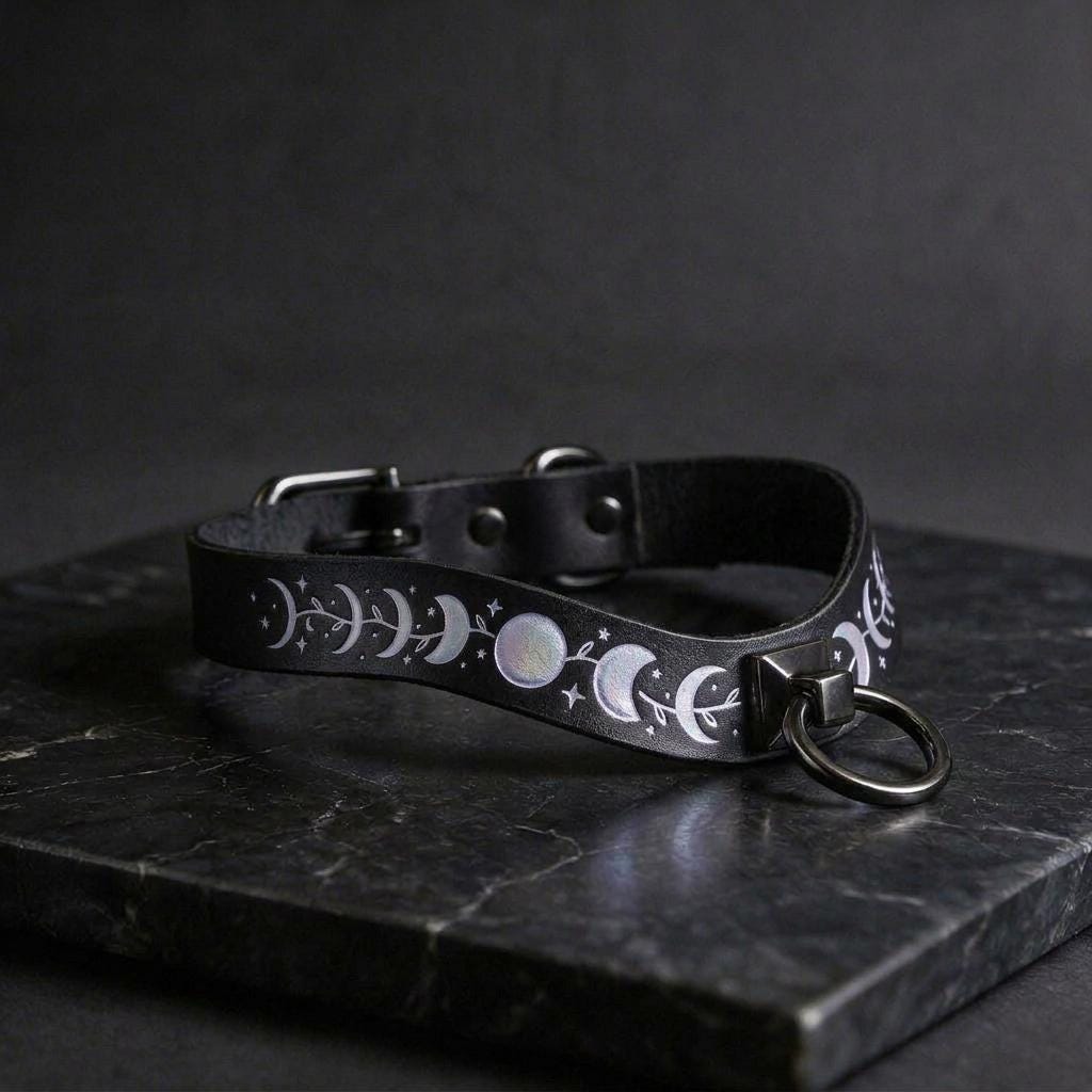 A black leather collar with moon and star designs on it, resting on a dark surface.