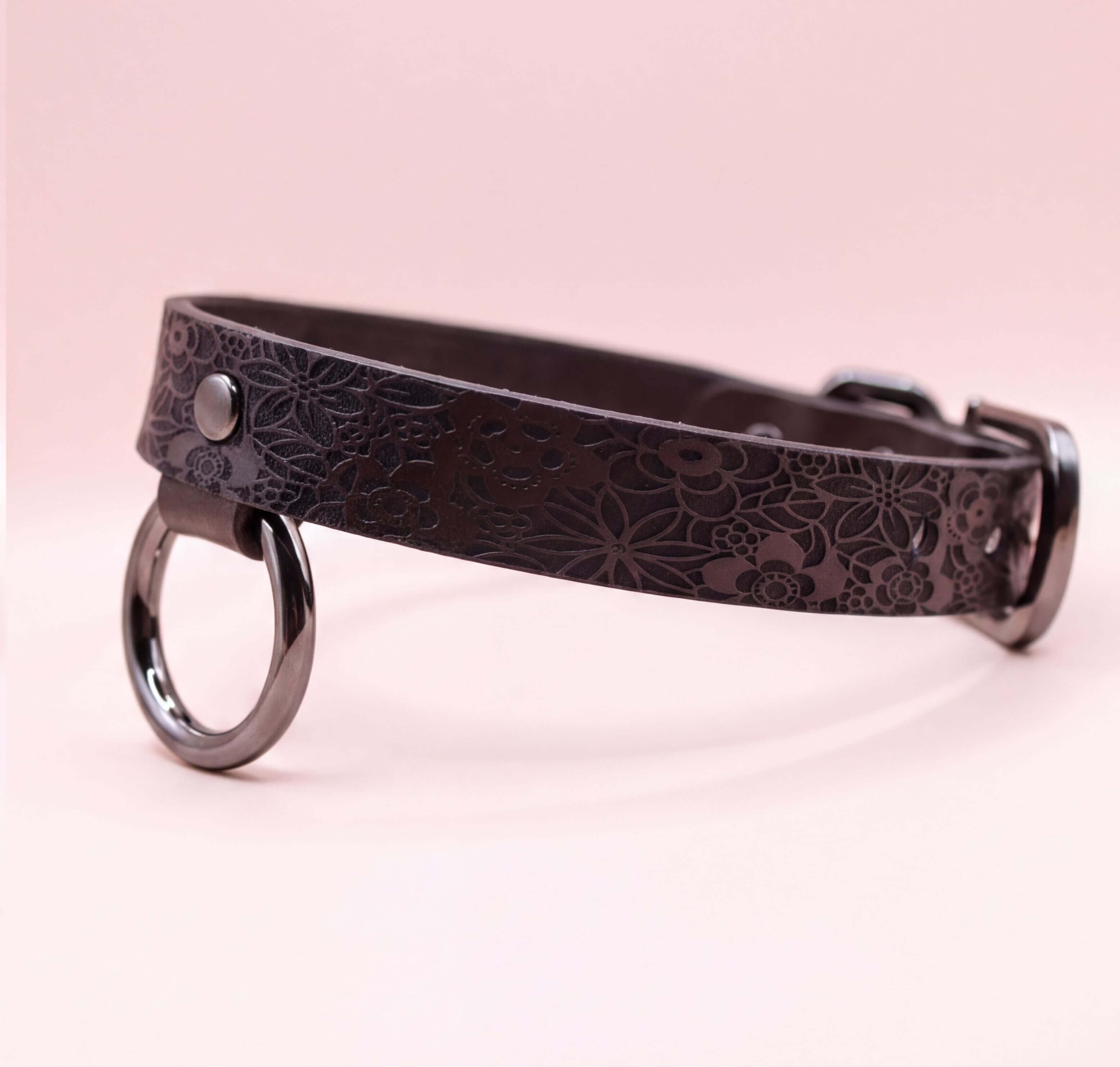 A black leather collar with a floral pattern and metal rings on the ends.