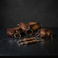 A set of brown leather straps with metal rings and buckles, arranged on a dark surface.