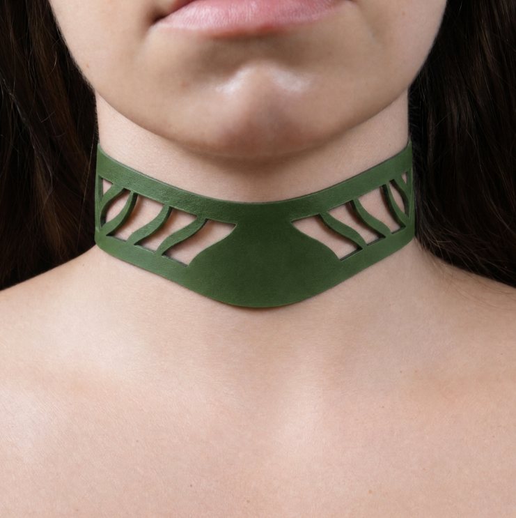 A close-up of a person's neck and chest area wearing a green choker necklace with a unique cutout design.