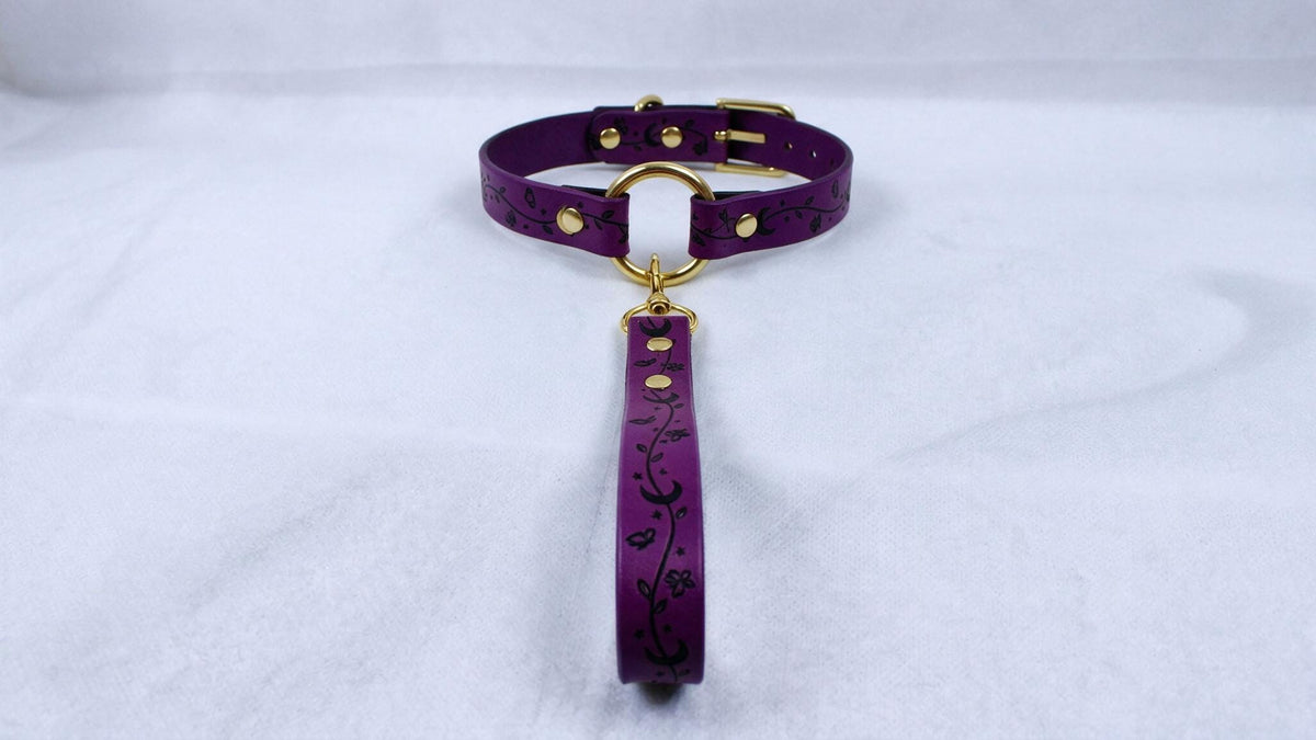 A purple leather collar with a gold-colored buckle and a floral pattern on the strap.