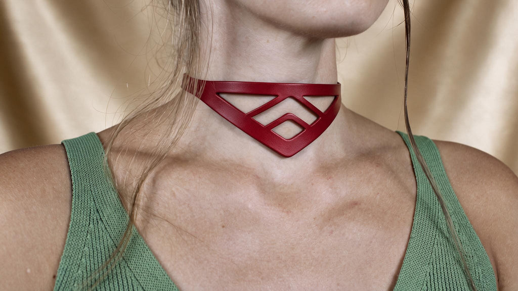 A close-up of a woman wearing a red choker necklace with a geometric pattern.