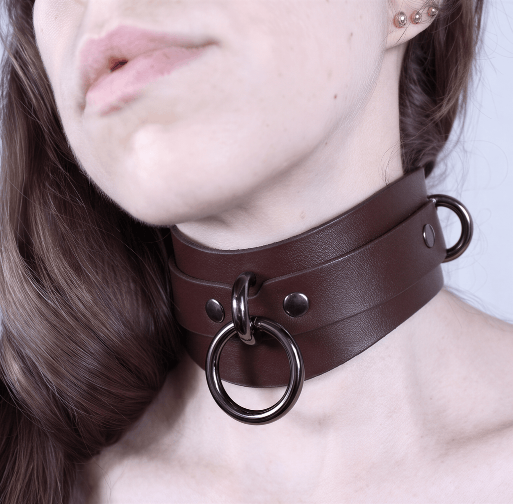 A close-up of a woman's neck wearing a brown leather choker necklace with metal rings.