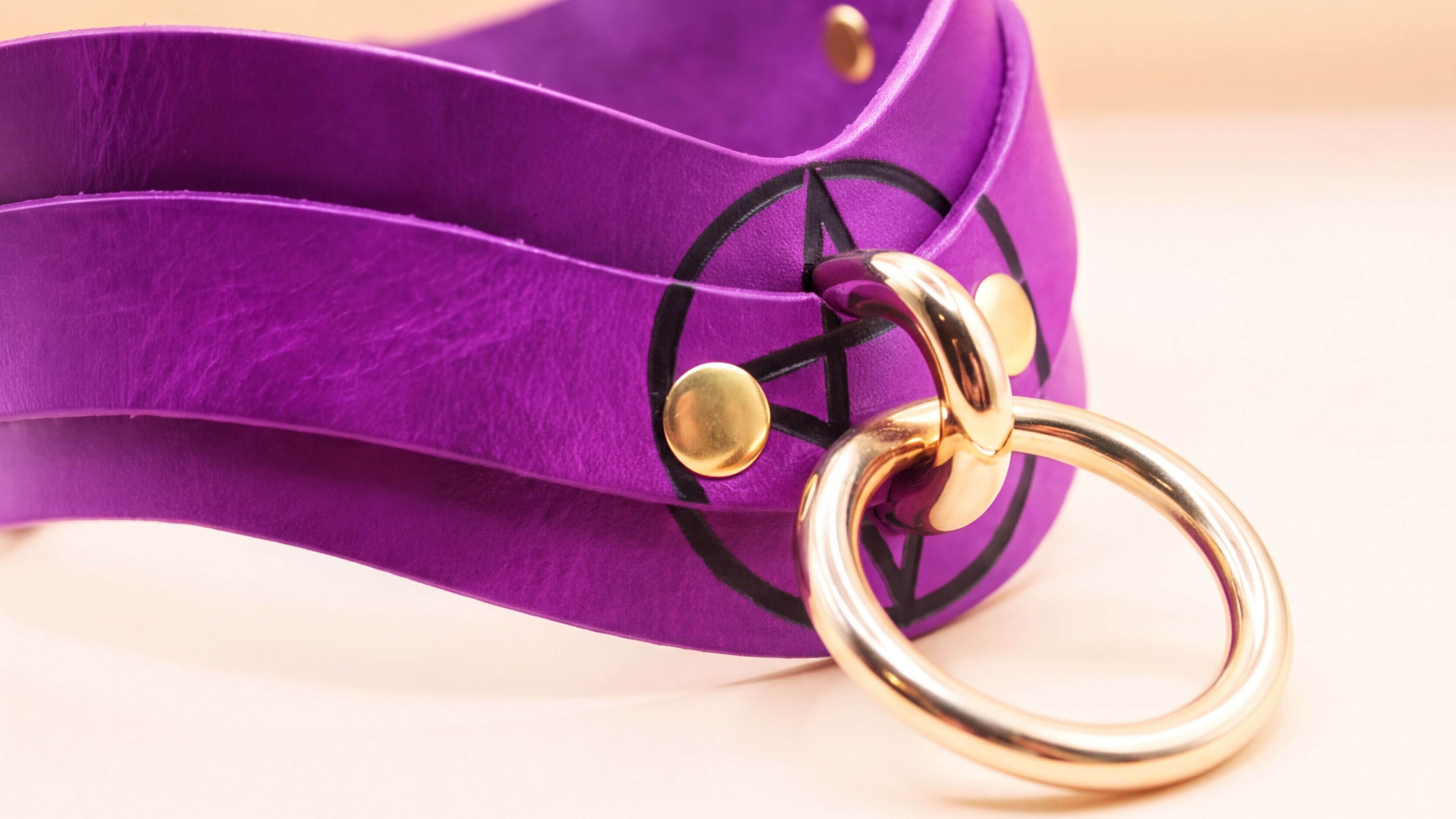 A purple leather choker necklace with a gold ring and a black symbol on it.