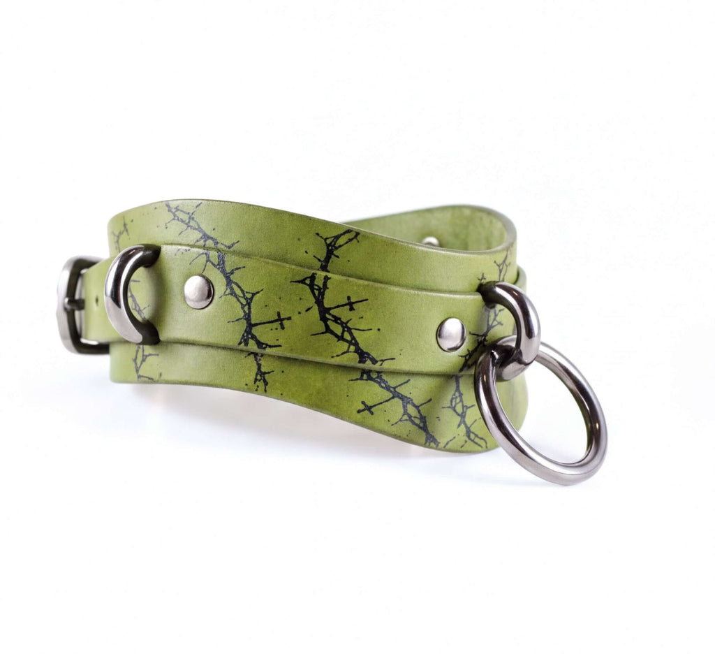 A green leather choker necklace with a black tree branch pattern and metal rings.