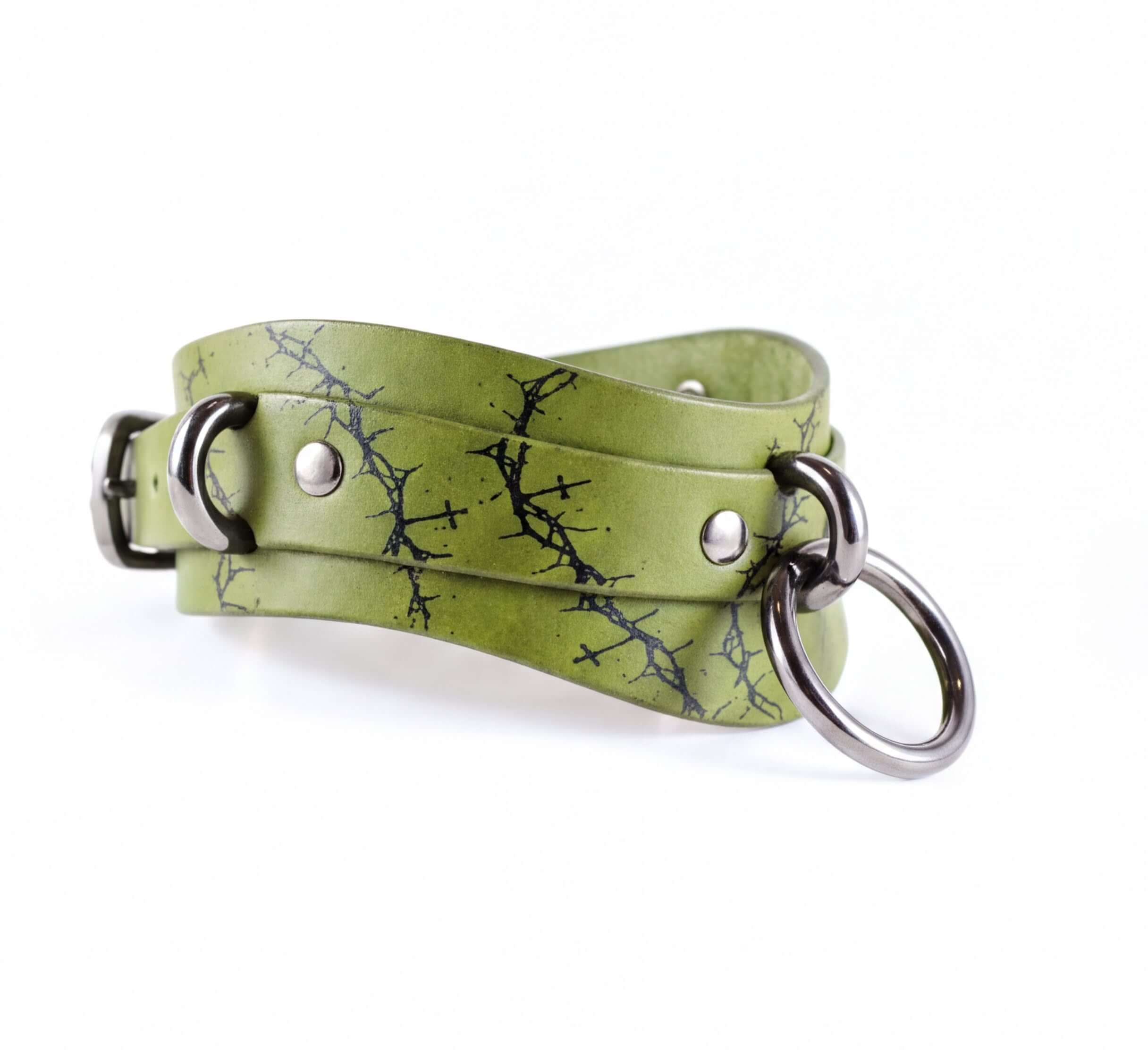 A green leather choker necklace with a black tree branch pattern and metal rings.
