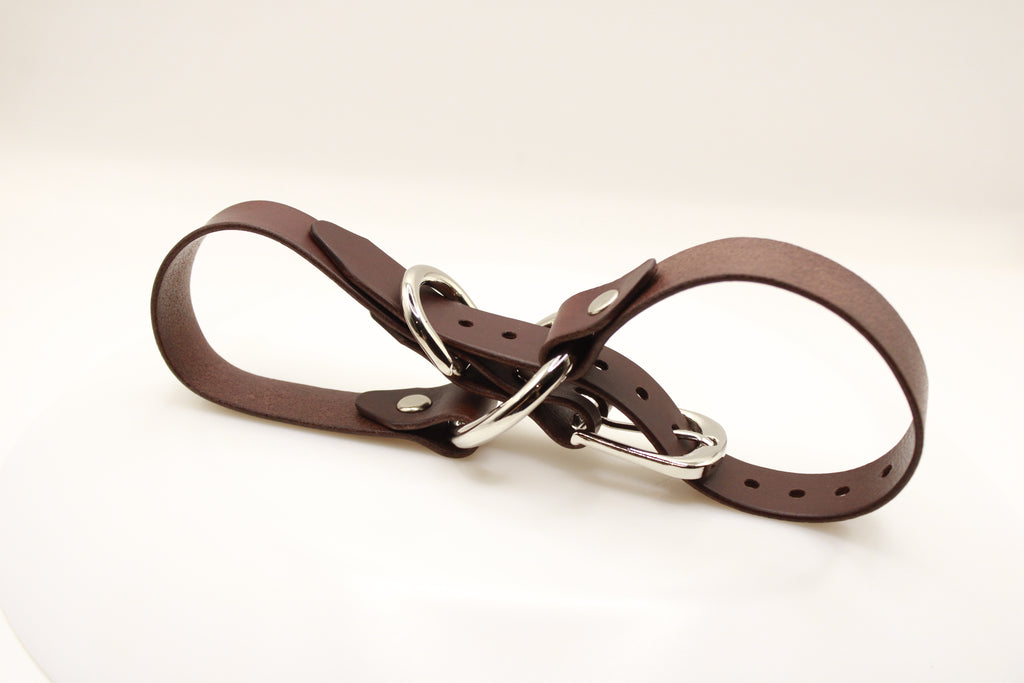 A brown leather strap with silver buckles and rivets, lying on a white surface.