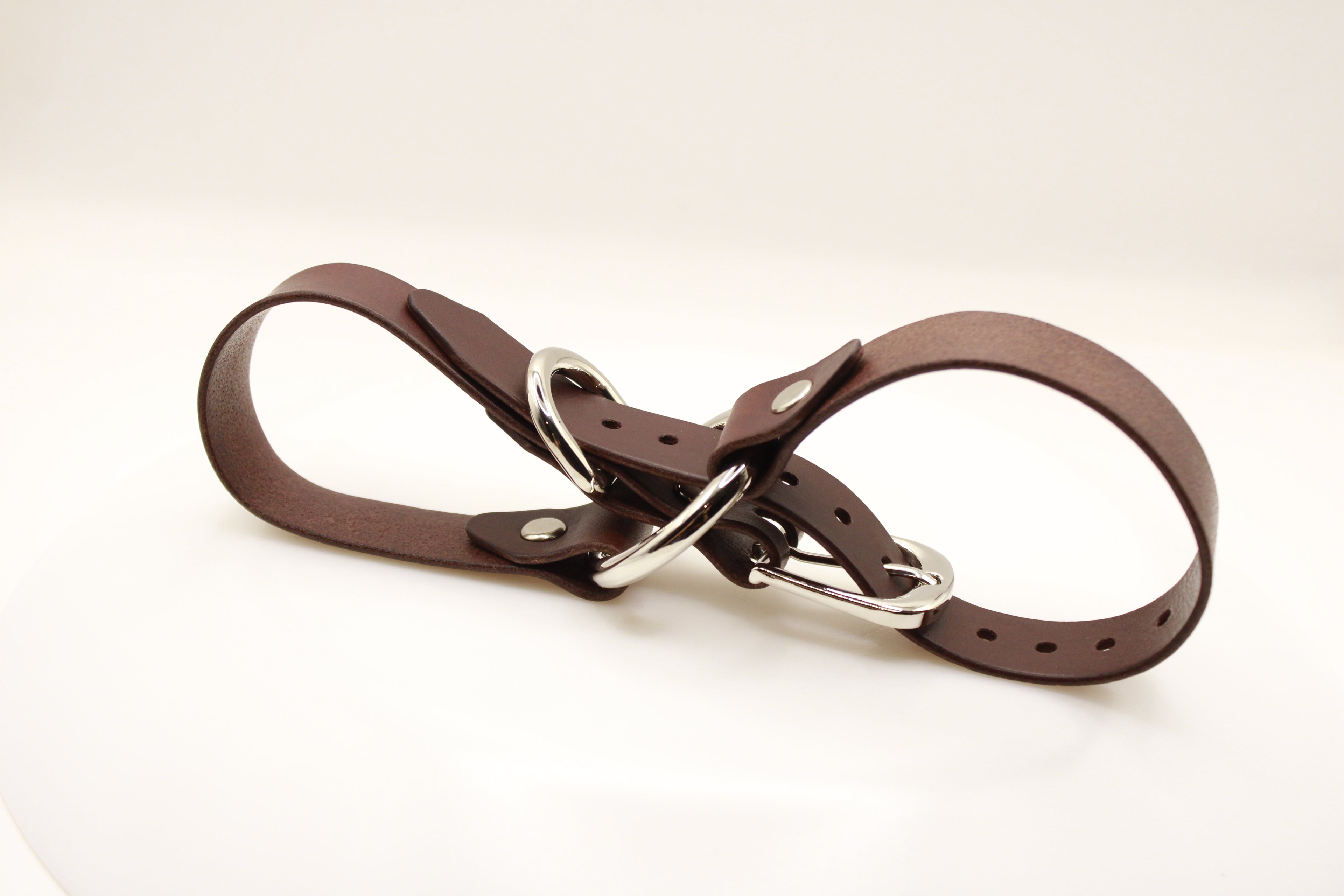 A brown leather strap with silver buckles and rivets, lying on a white surface.