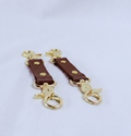 a pair of brown leather straps with gold-colored metal clasps, placed on a white surface.