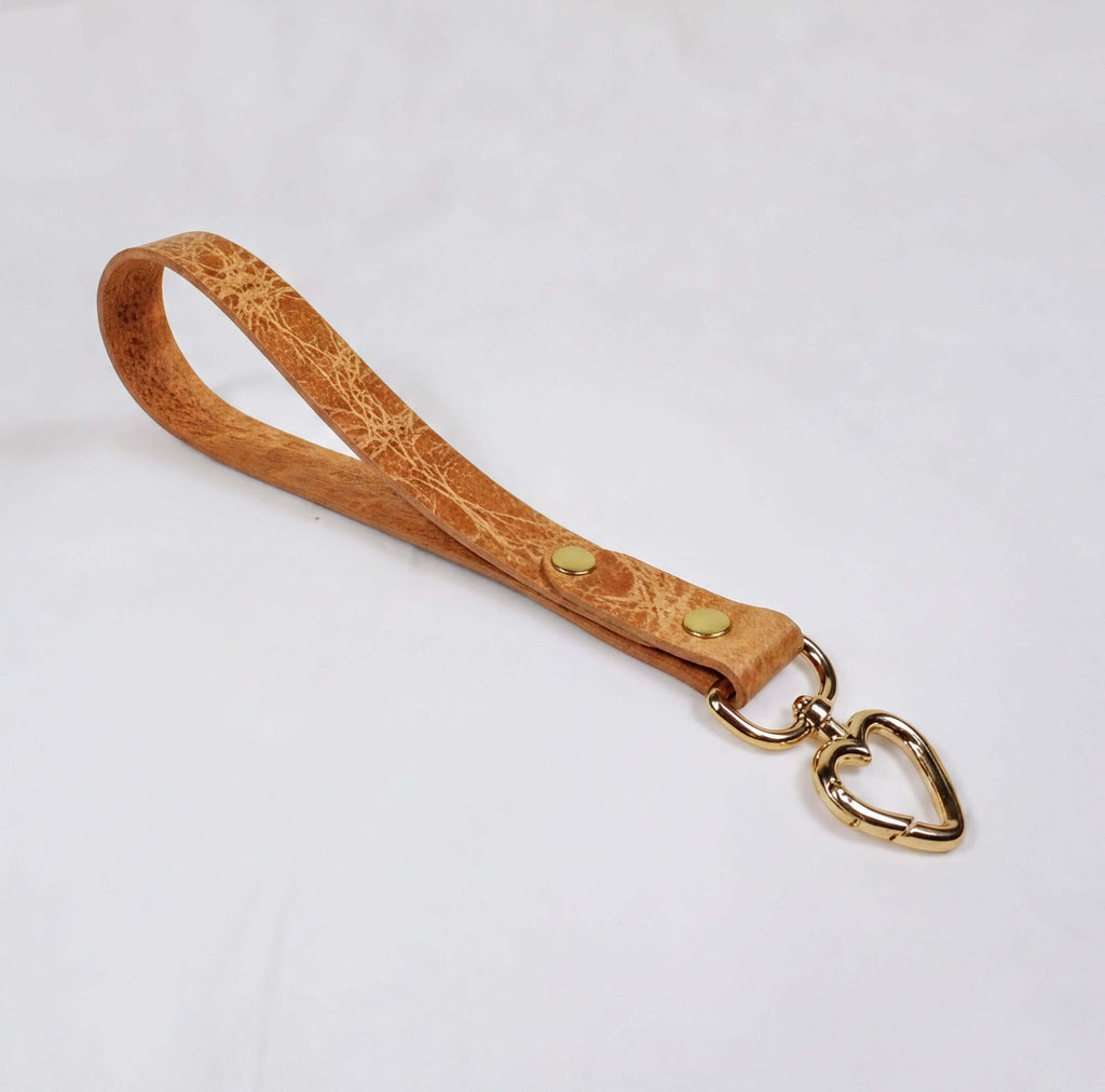 A tan leather strap with a heart-shaped metal clasp attached to it.