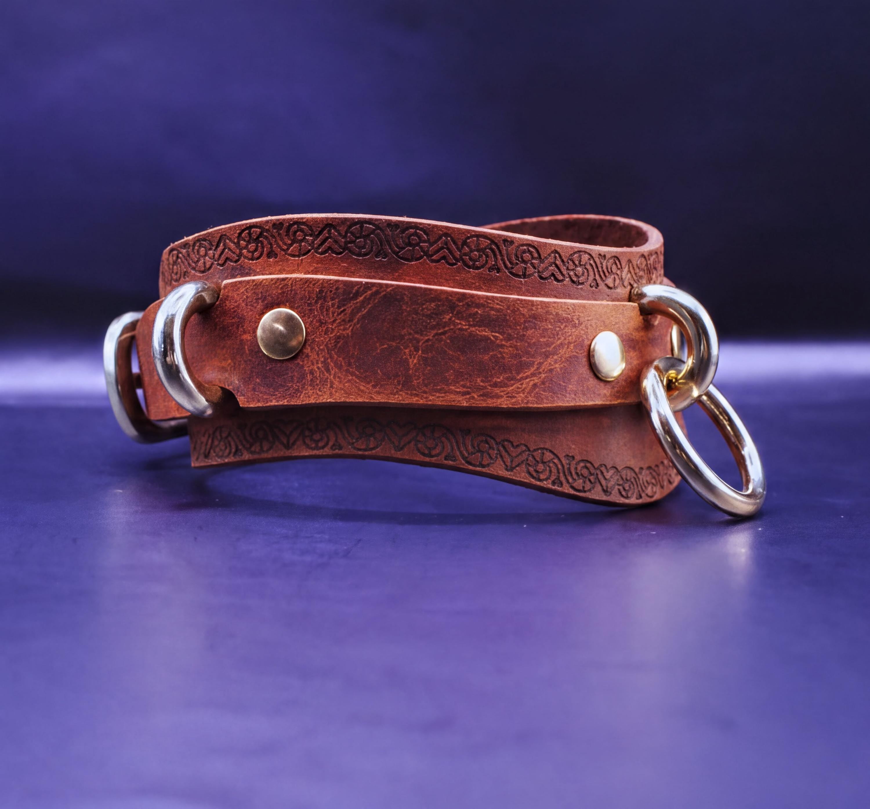 A brown leather strap with metal rings and a decorative pattern on it, resting on a blue surface.