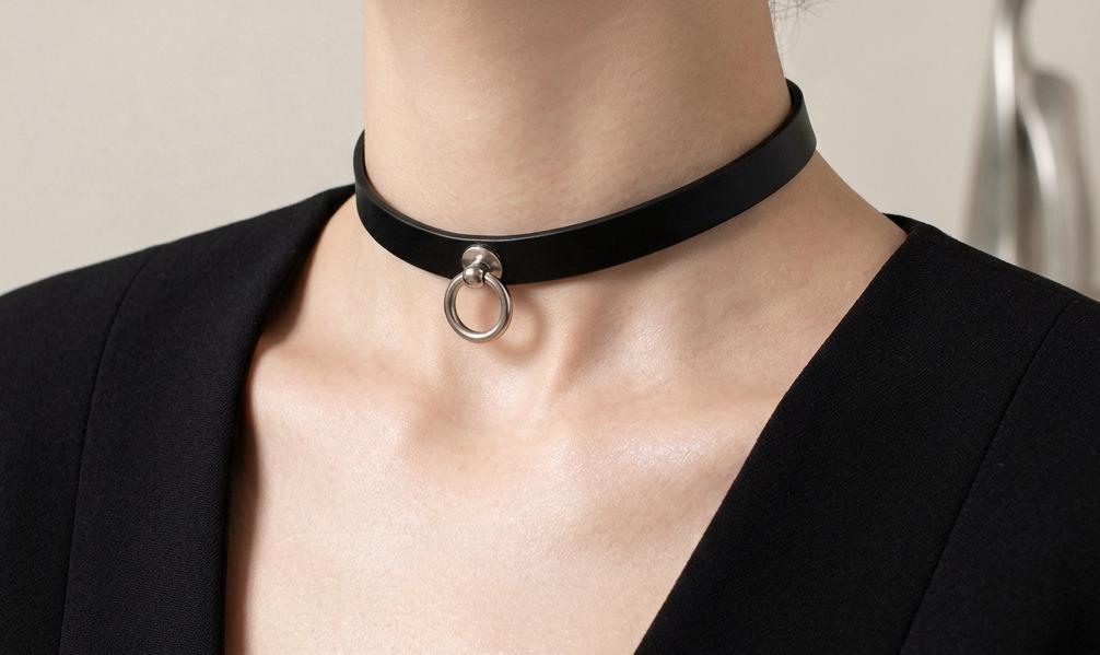 A close-up of a person wearing a black choker necklace with a metal ring.