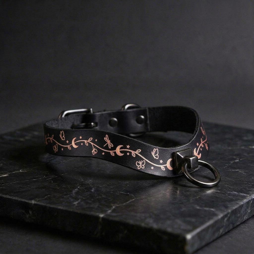 A black leather collar with a decorative pattern on it, resting on a dark surface.
