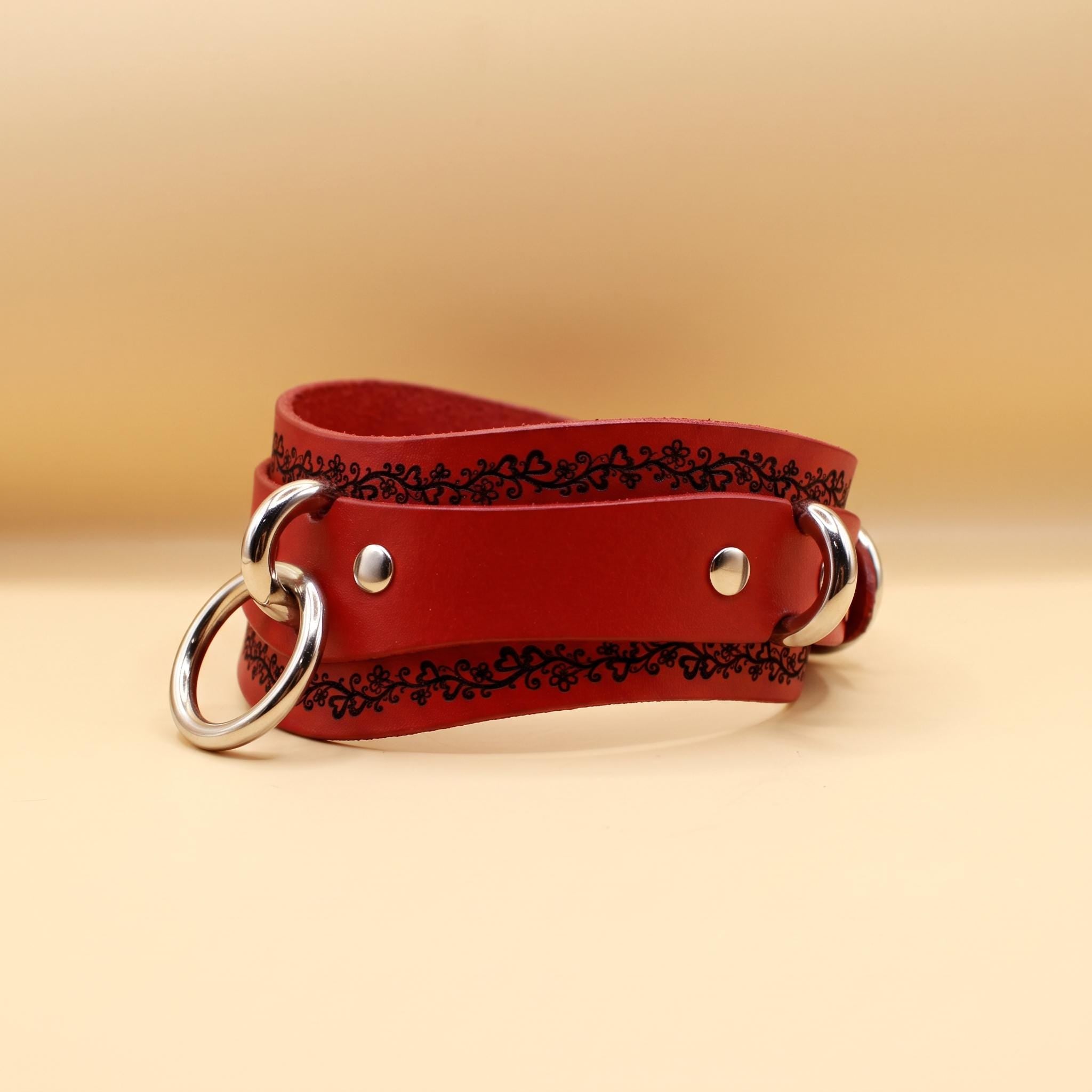 A red leather choker necklace with metal rings and a decorative pattern on the front.