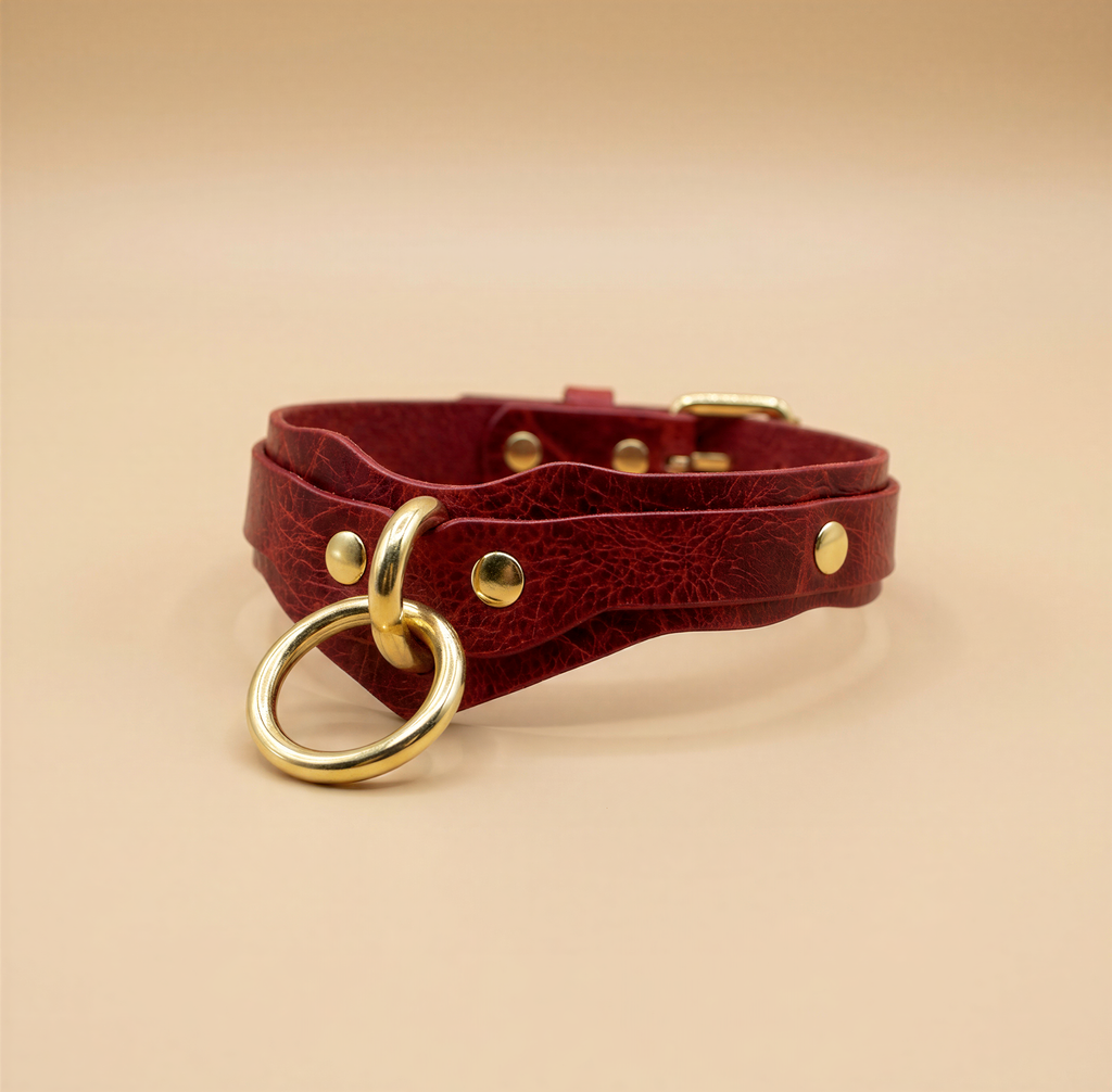 A red leather choker necklace with a gold ring and metal studs.