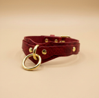 A red leather choker necklace with a gold ring and metal studs.