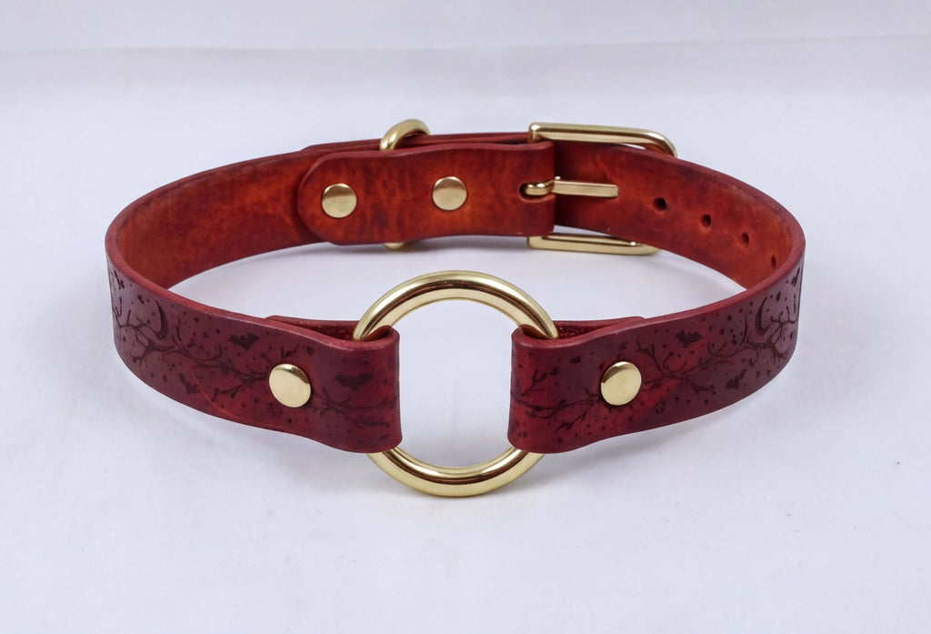 A burgundy leather collar with a gold-colored metal ring and buckle.