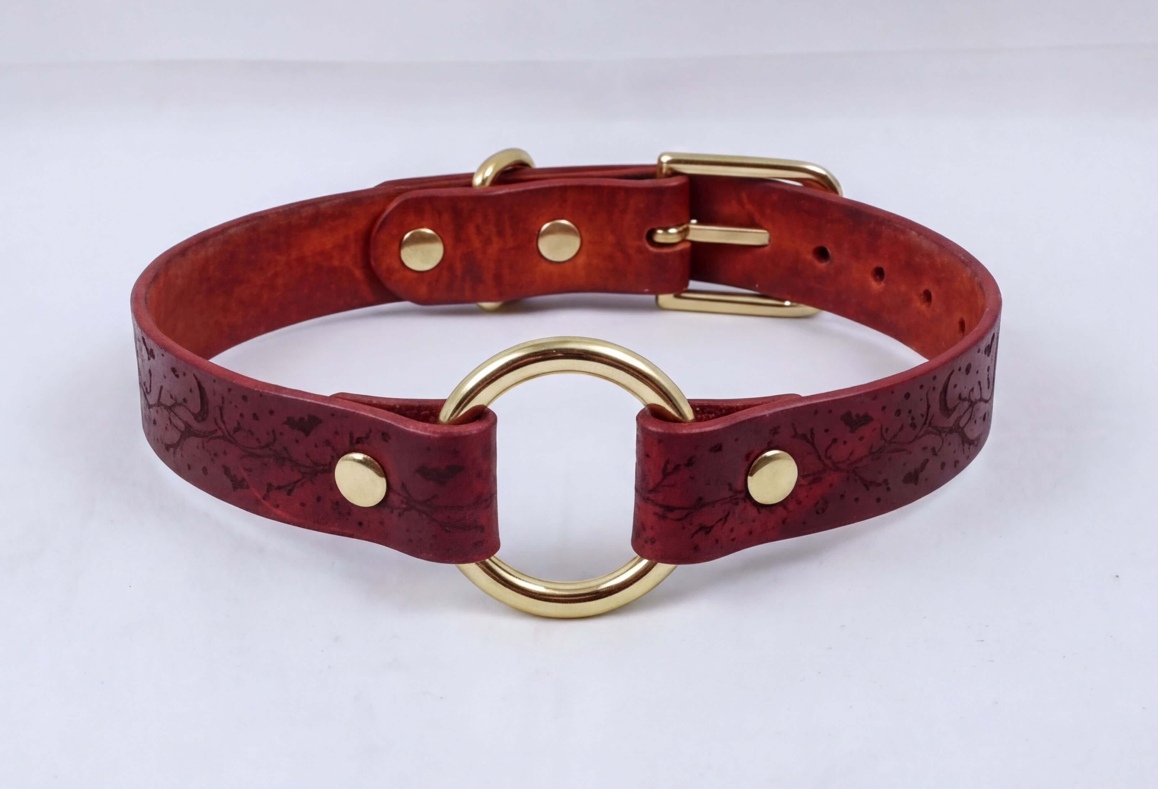 A burgundy leather collar with a gold-colored metal ring and buckle.