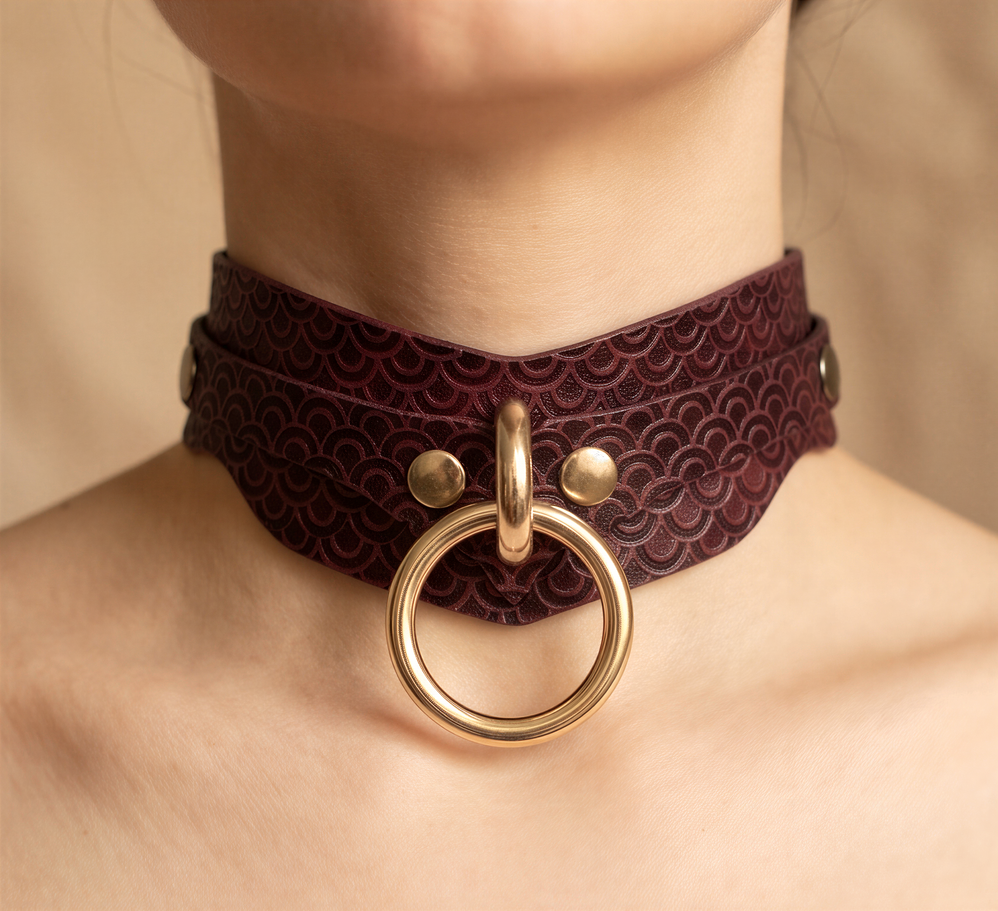 A close-up image of a person wearing a burgundy choker necklace with a gold ring and two gold buttons.