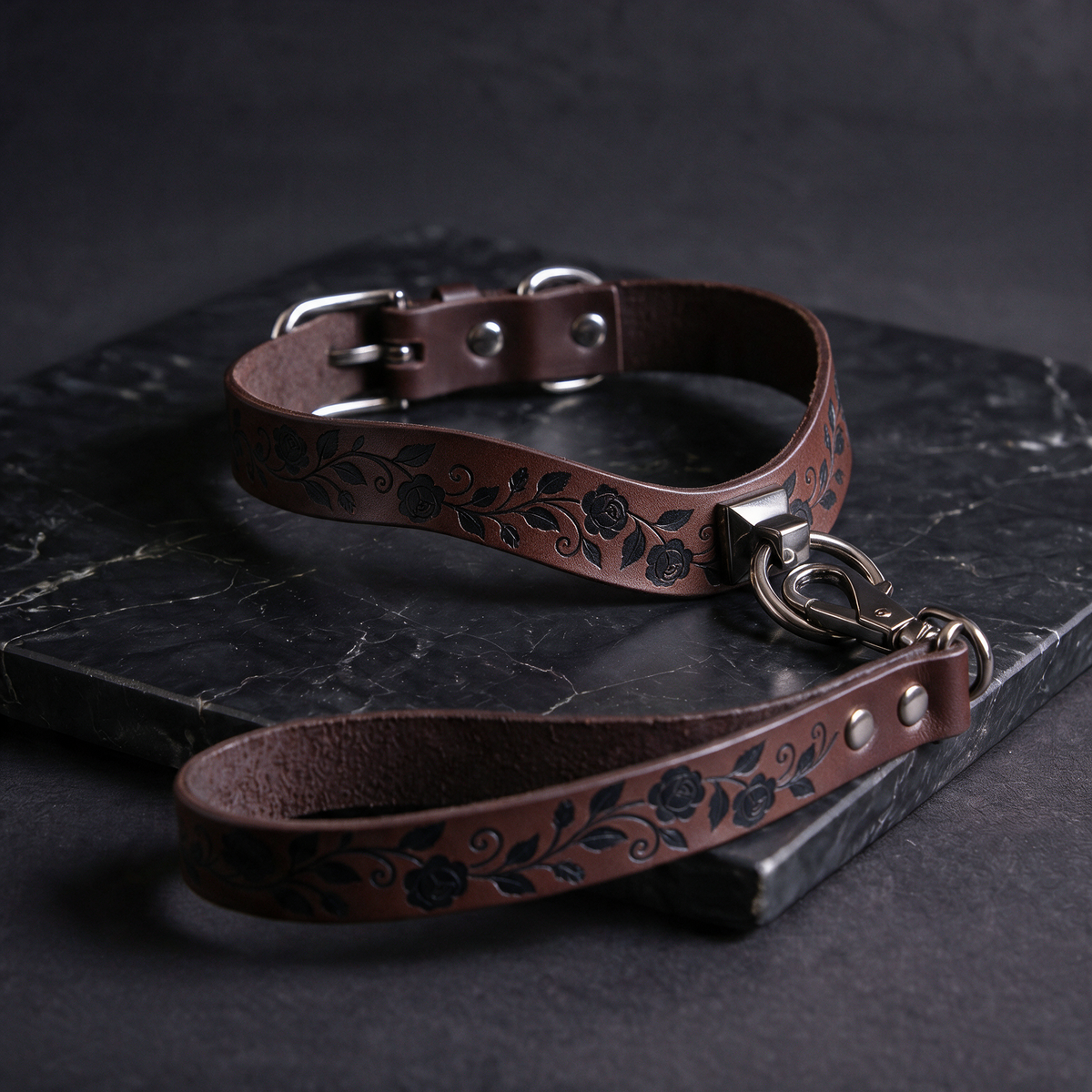 A brown leather collar with a floral pattern and a metal clasp, resting on a dark surface.