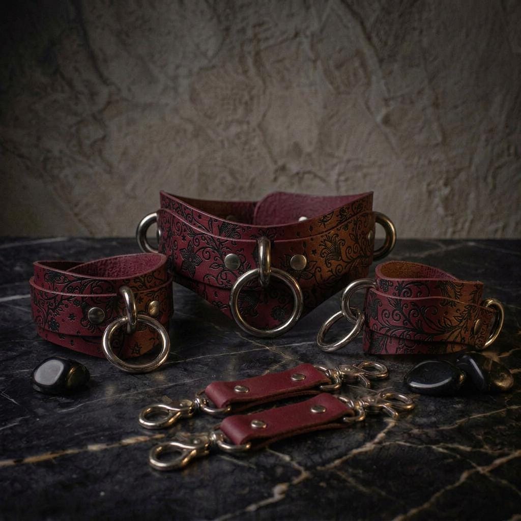 a collection of leather straps and accessories, including a large burgundy leather strap with metal rings and a smaller one, as well as some additional accessories, all arranged on a dark surface.