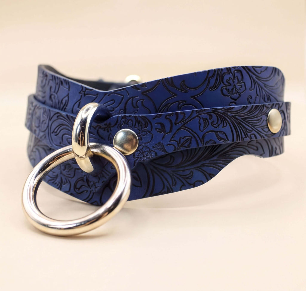 A blue leather choker necklace with a silver ring and two metal studs on the front.
