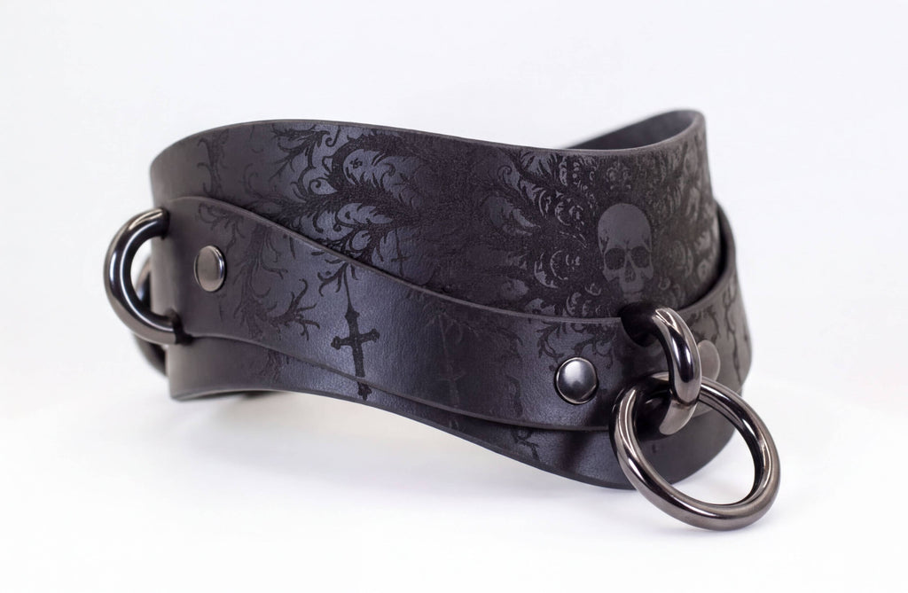 A black leather choker with a skull design and metal rings on the ends.