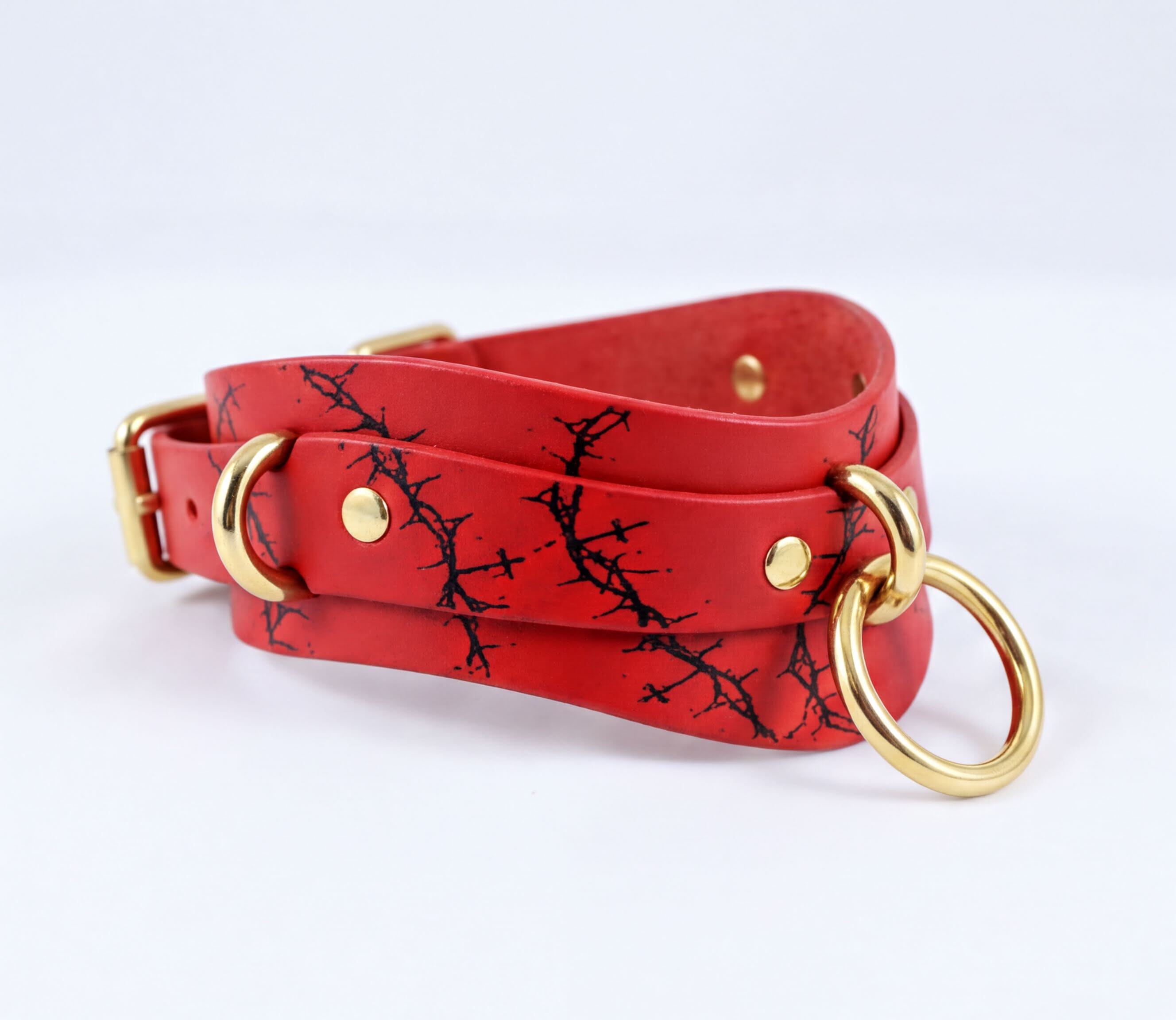A red leather choker necklace with a black tree branch pattern and gold-colored metal rings.