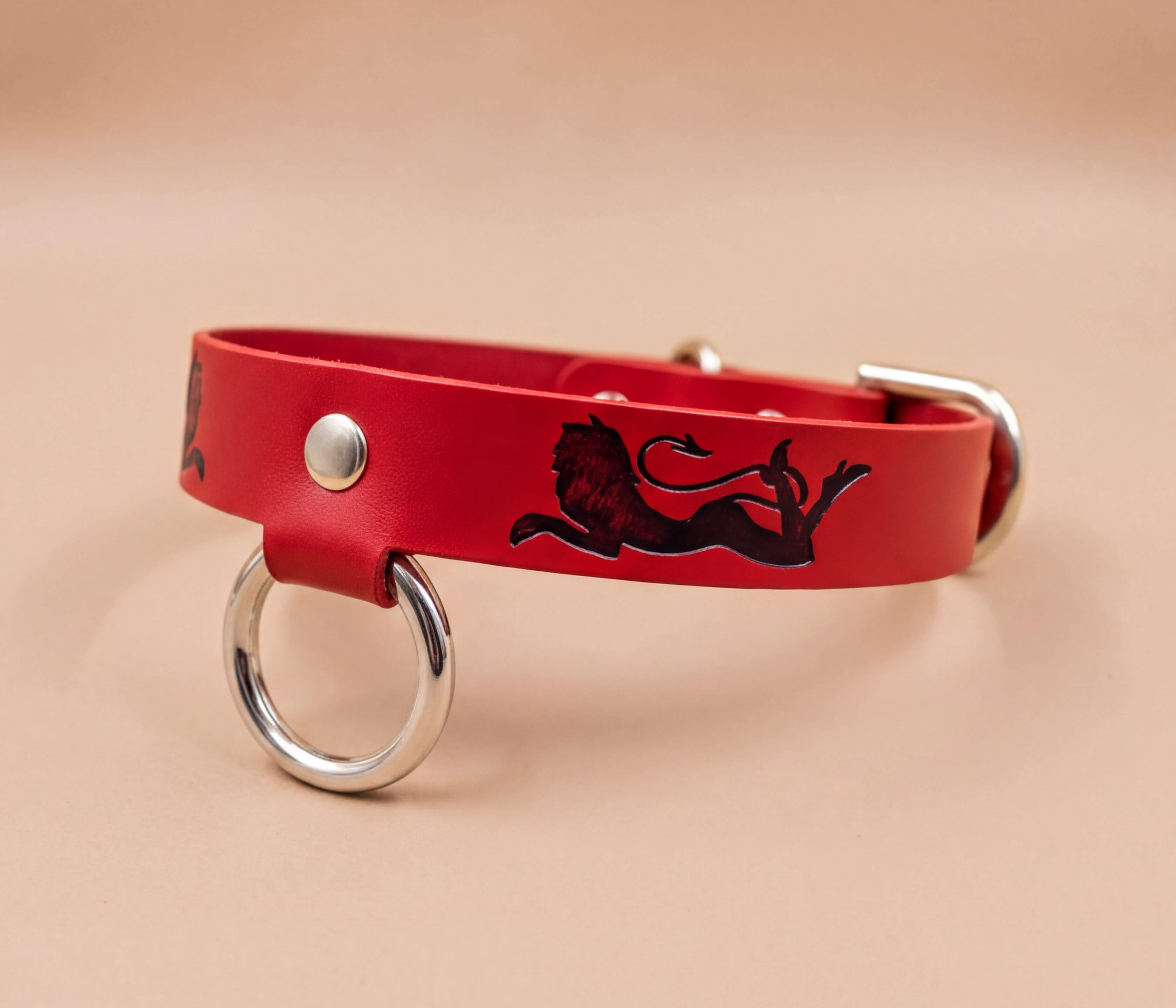 A red leather dog collar with a lion design and metal ring.