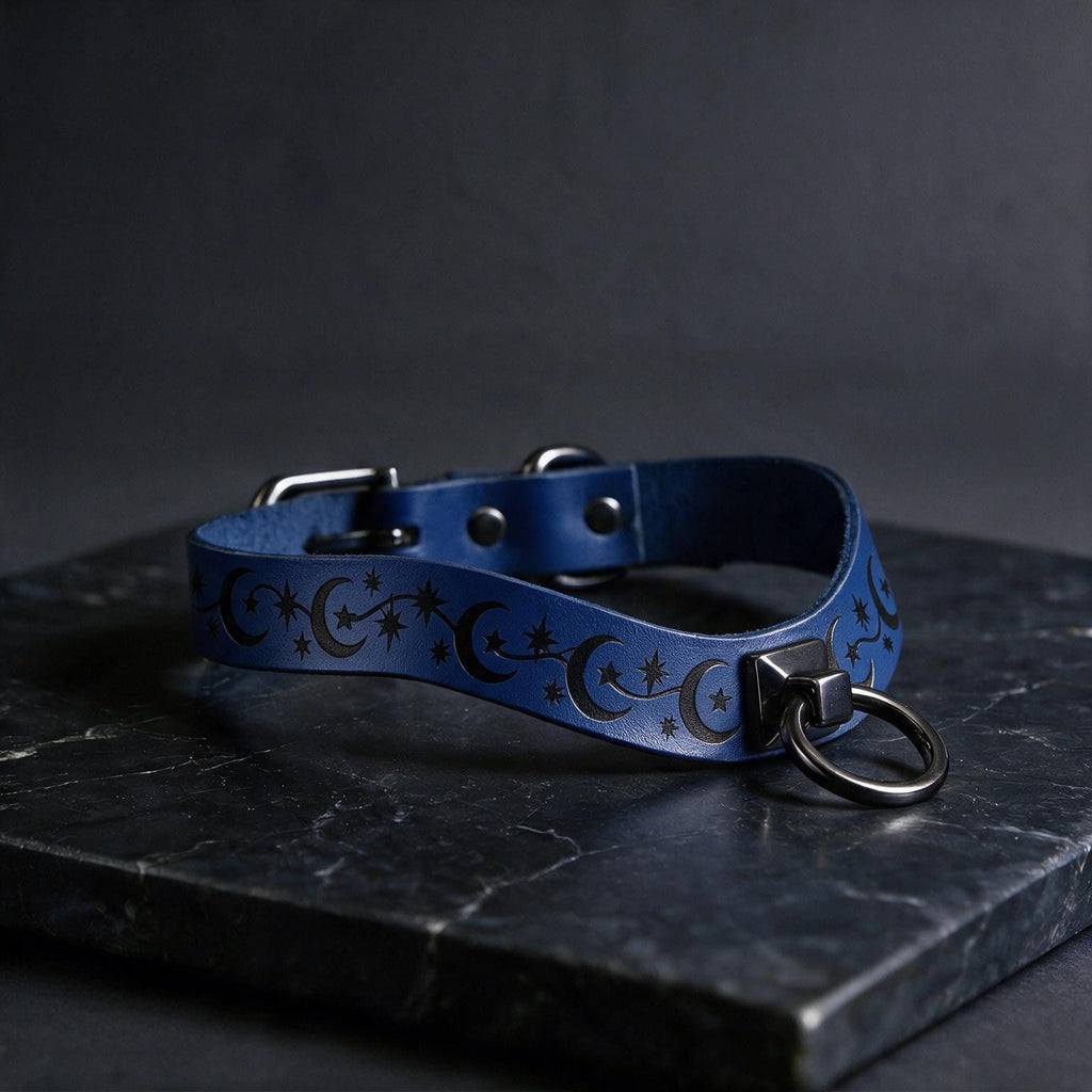 A blue leather collar with a star and crescent design, featuring a metal ring and buckle, is displayed on a dark surface.