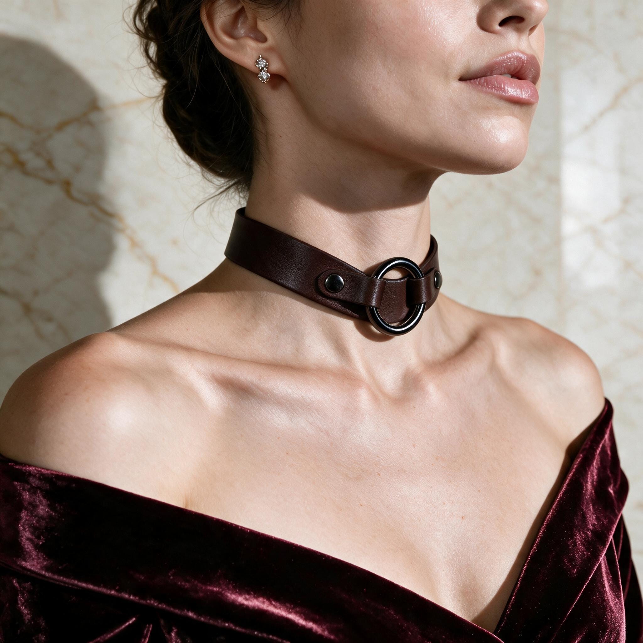 A woman wearing a brown leather choker necklace with a circular buckle, and a burgundy velvet off-the-shoulder dress.