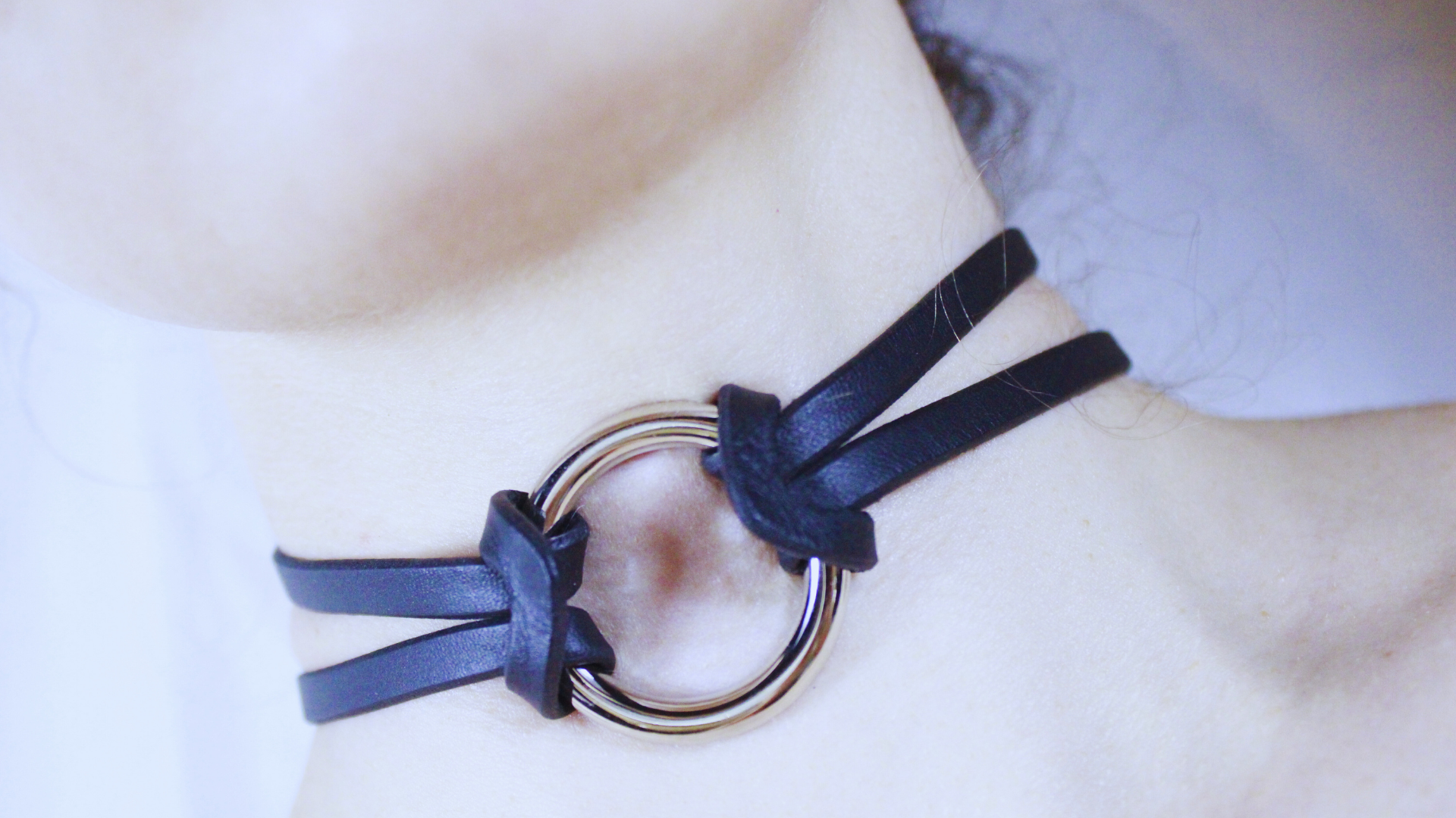 A close-up view of a person's neck and chin area, featuring a dark blue leather choker necklace with a metal ring.