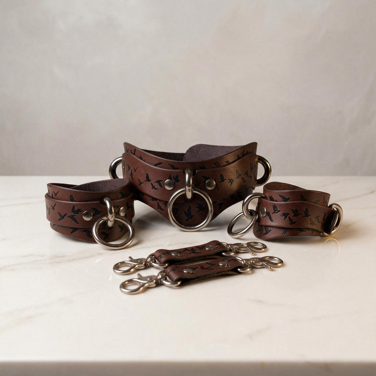 A set of brown leather straps with metal rings and buckles, arranged on a white marble surface.
