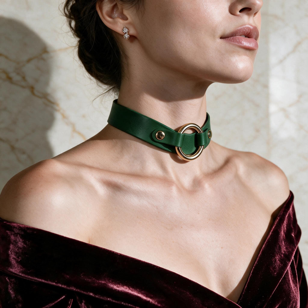 A woman wearing a green choker necklace with a gold ring, posing against a marble wall.