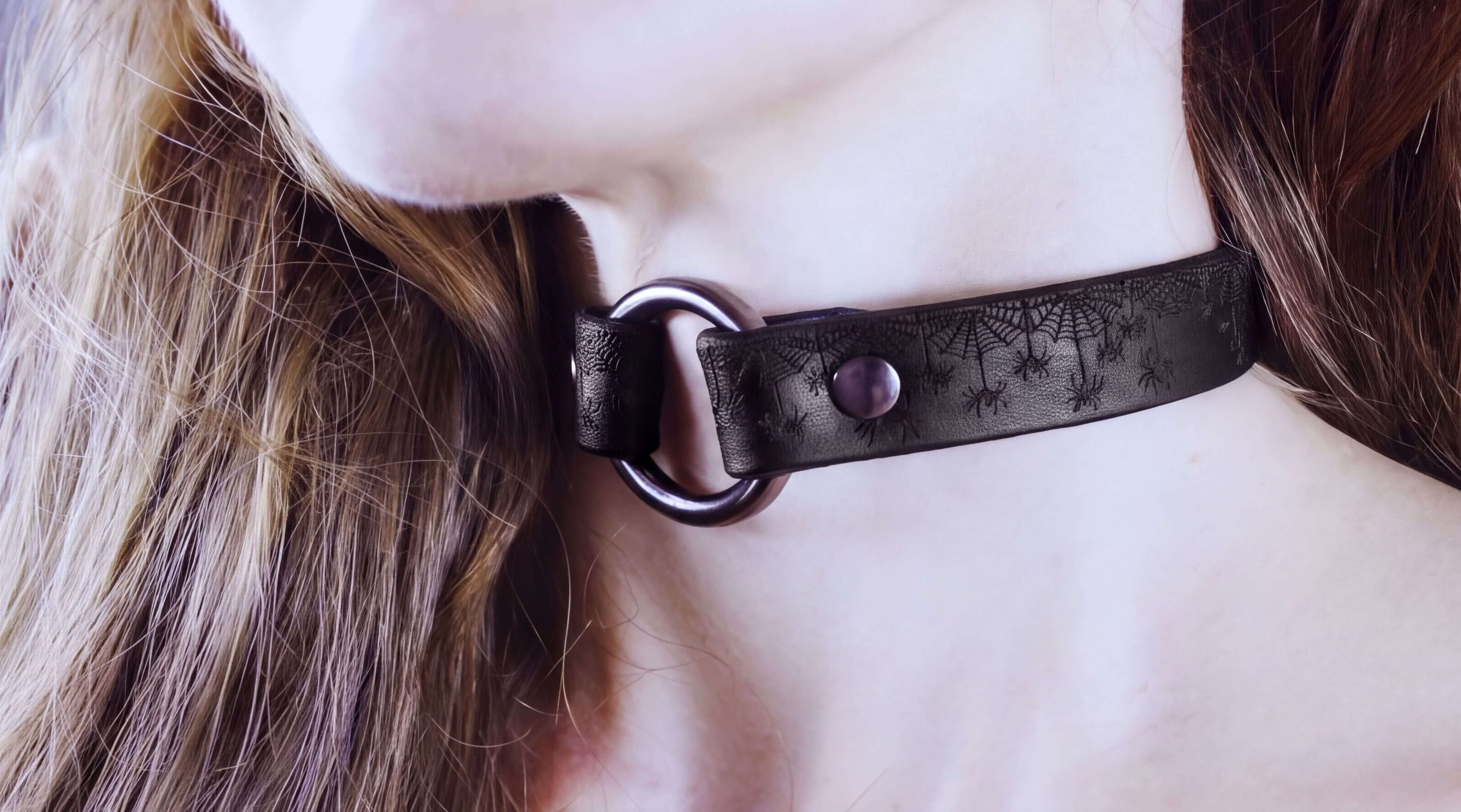 A close-up of a person's neck and chin wearing a black choker necklace with a spider web design.