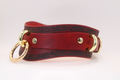 A red leather choker necklace with gold-colored metal rings and a decorative pattern on the leather.
