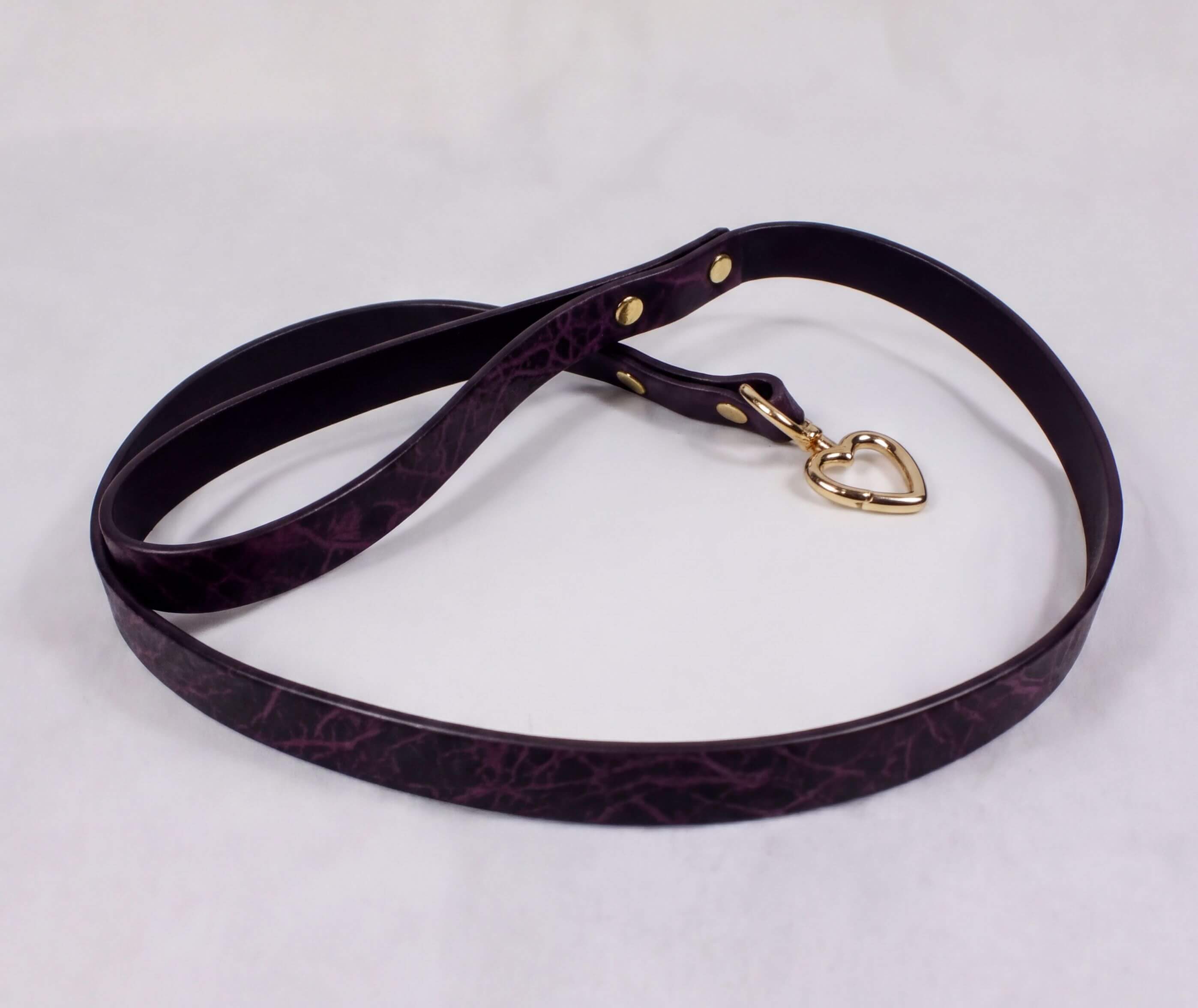 A purple leather leash with a gold heart-shaped tag attached, lying on a white surface.