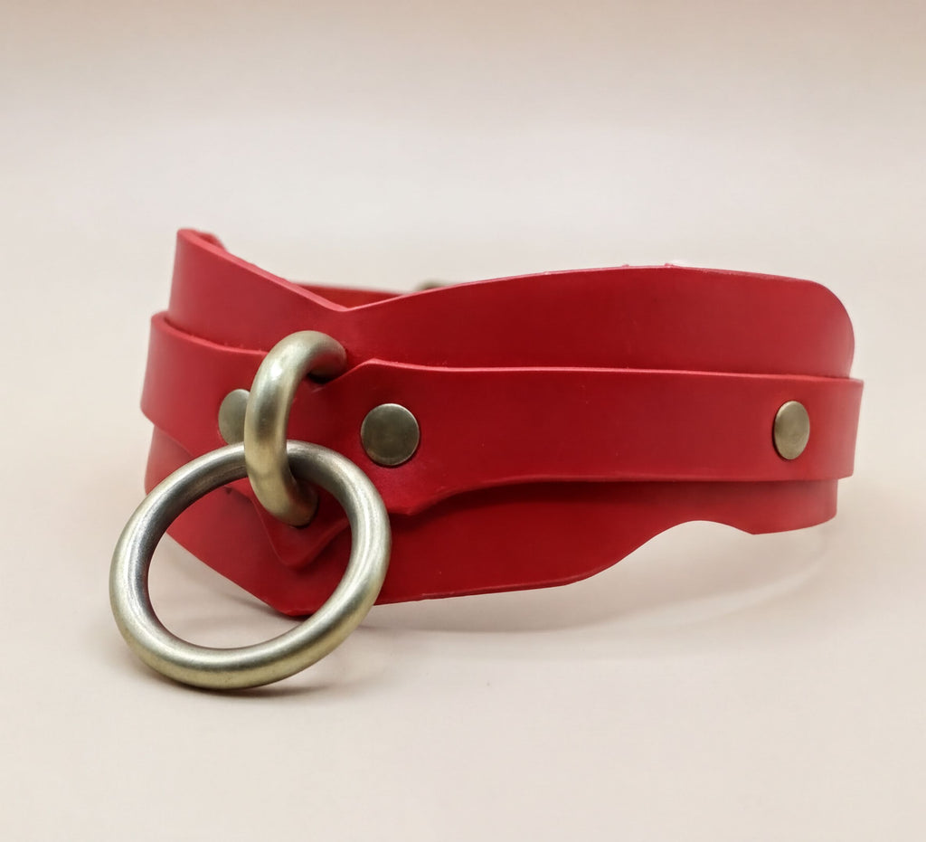 A red leather choker necklace with a metal ring and two metal studs on the front.