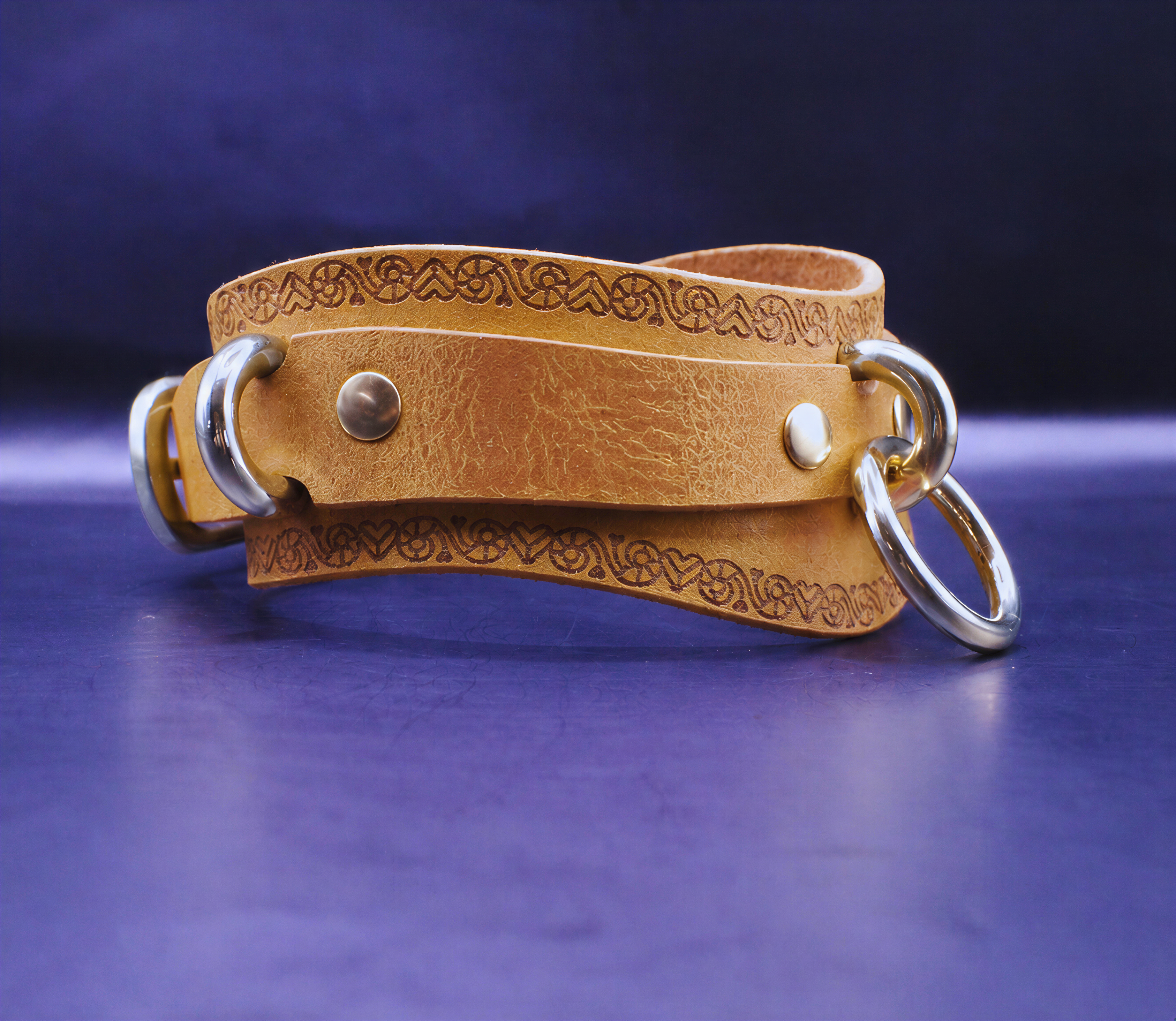 A tan leather strap with metal rings and decorative patterns is displayed against a dark blue background.