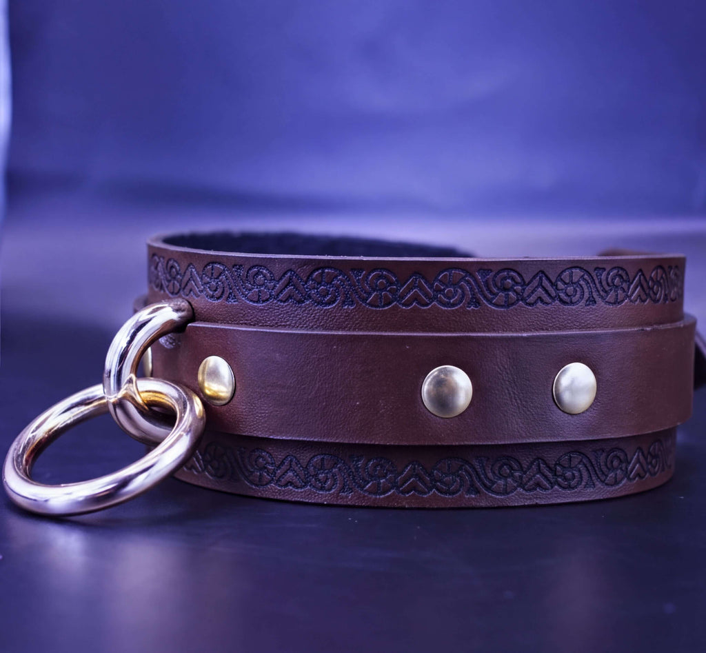 A brown leather choker necklace with a decorative metal ring and three metal buttons on the front.