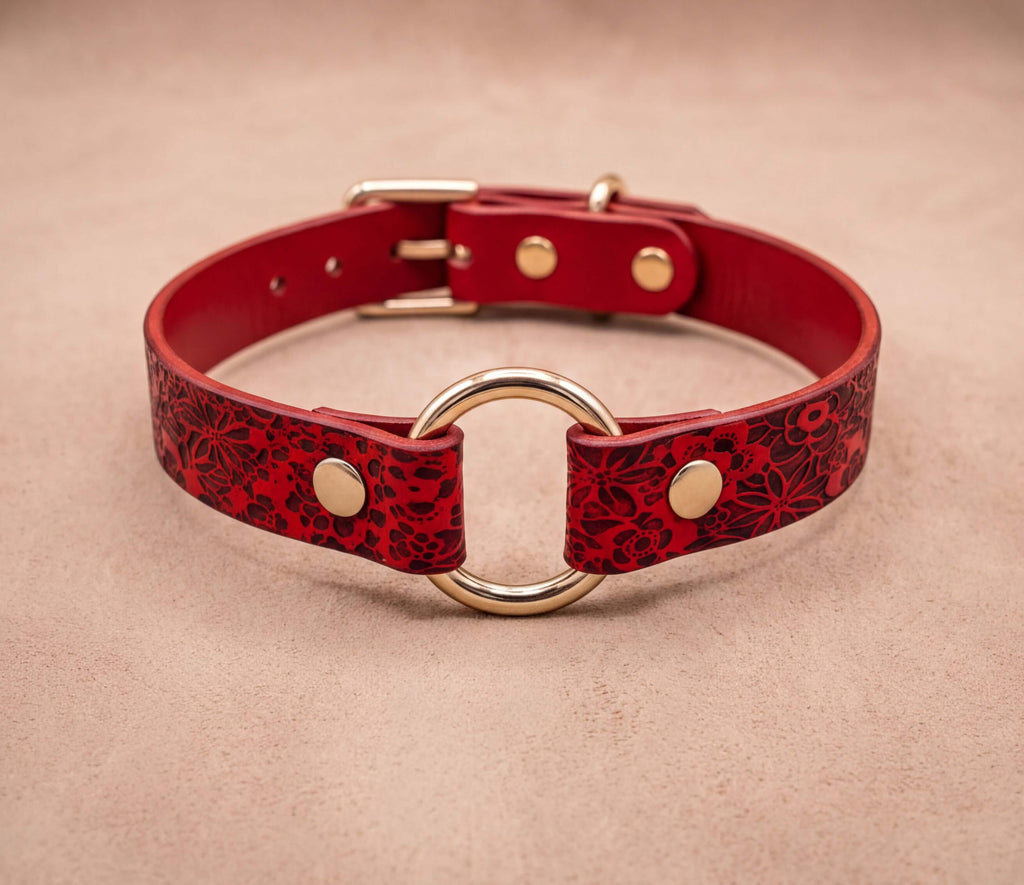 A red leather collar with a gold ring and buckle, featuring a floral pattern.