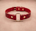 A red leather collar with a gold ring and buckle, featuring a floral pattern.