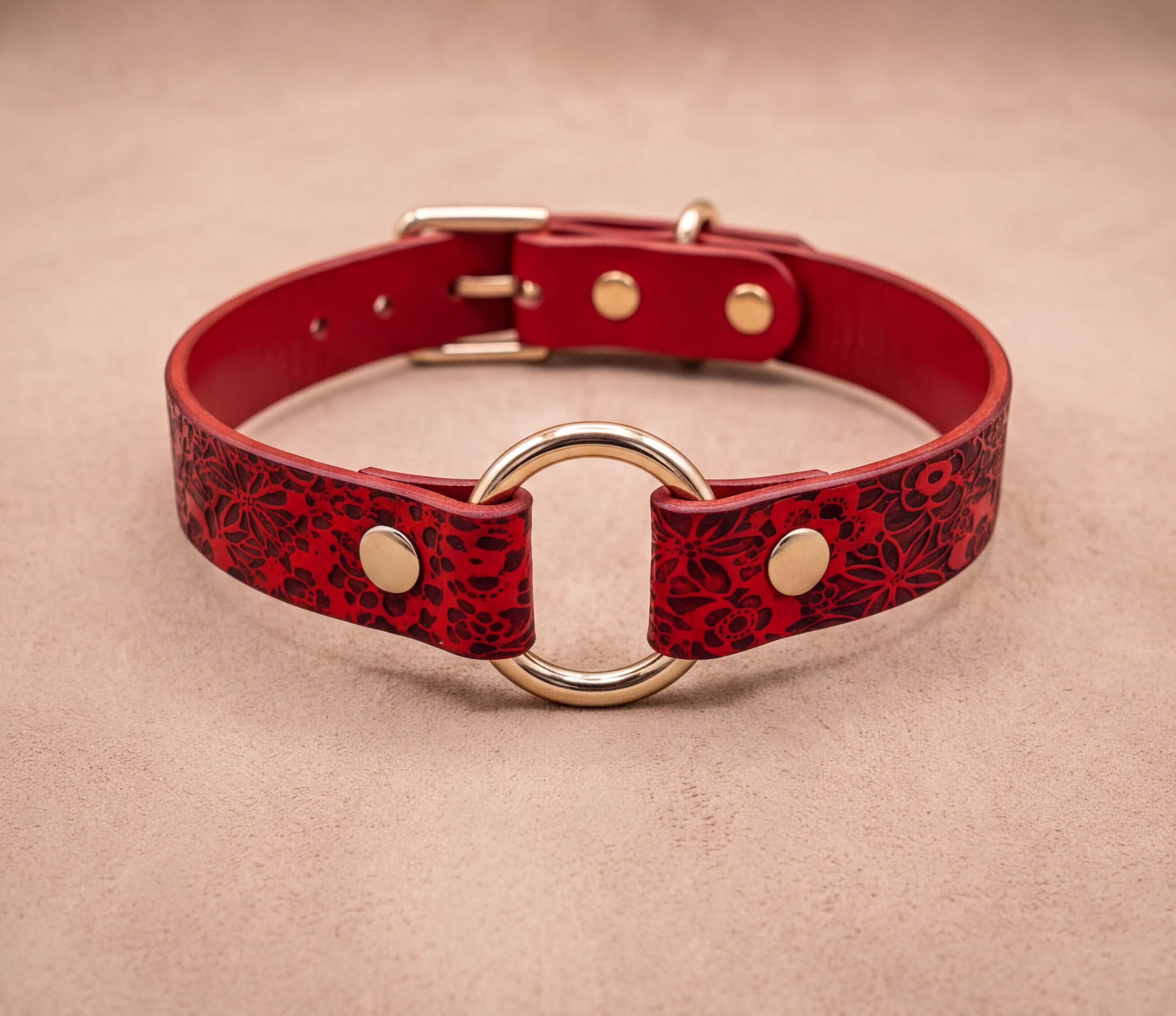 A red leather collar with a gold ring and buckle, featuring a floral pattern.
