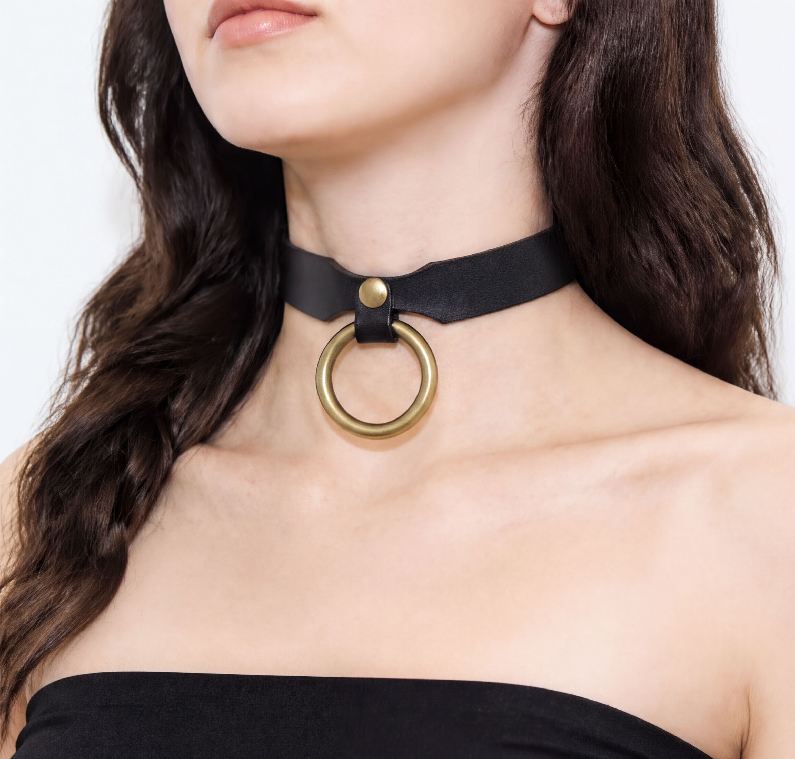 A close-up of a woman's neck and chest area wearing a black choker necklace with a gold ring.